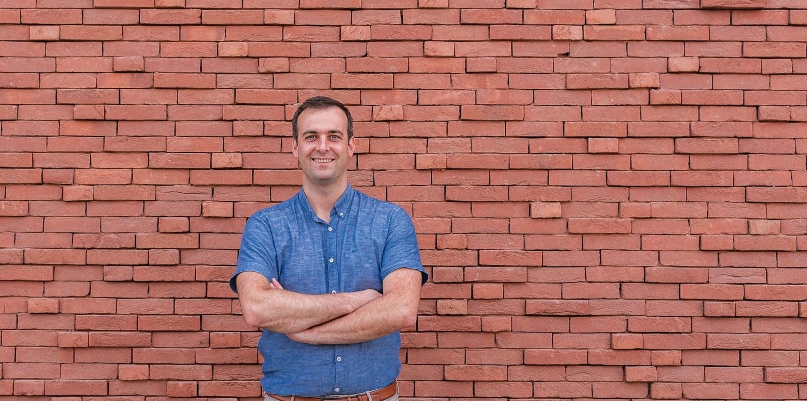 Dr. Karel Anseeuw, huisarts, staat met gekruiste armen voor een bakstenen muur
